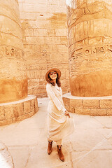 Fototapeta na wymiar Happy woman traveler explores the ruins of the ancient Karnak temple in the heritage city of Luxor in Egypt. Giant row of columns with carved hieroglyph