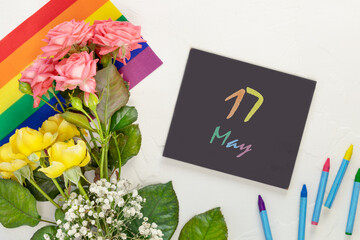 Lgbt composition with pink and yellow roses on a rainbow flag and chalkboard with inscription 17...