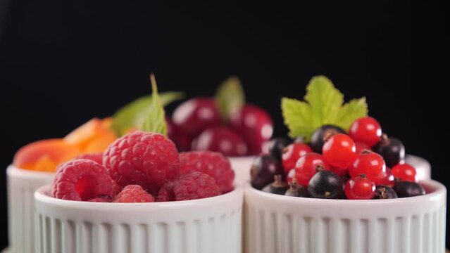 Assorted summer fruits in small cups in a circle spinning on dark background. Fresh juicy fruit desserts with leaves decoration - healthy summer snack.