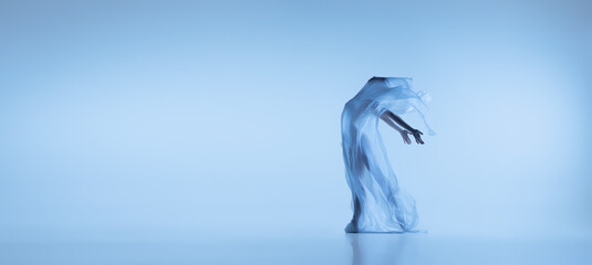Portrait of flexible woman, graceful ballerina dancing with fabric, cloth isolated on blue studio...