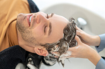 Male customer sitting at the chair in the beauty salon and having his hair washed