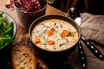 Finnish creamy soup with salmon, potatoes, onions, and carrots in a bowl on the wooden table, selective focus