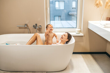 Joyful mother playing with her baby in the bathtub