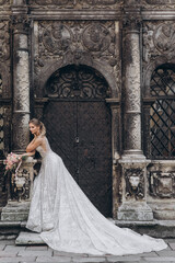 Fototapeta premium Beautiful bride in a long white wedding dress on a background of black old building