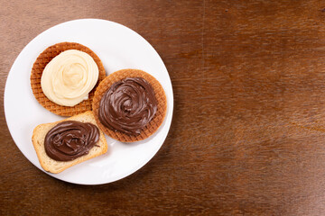 toast and waffles with chocolate, hazelnut and white chocolate creams top view on white plate on wooden table