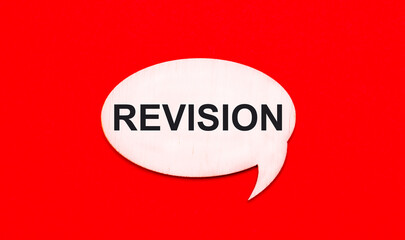 On a bright red background, a light wooden curly card with the text REVISION