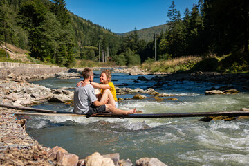A lovely couple is enjoying time together on a thin desk over a river in the mountains