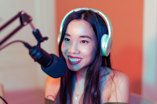 smiling asian woman podcasting with microphone and headphones