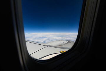 Naklejka premium View through the window of a plane of the wing and turbine during a flight on a beautiful blue sky day with white clouds, flying high.