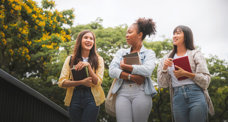 Three young college student holding books walking and talking in the garden.