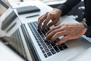 Male hands typing on laptop keyboard closeup