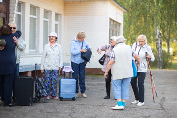 A group of elderly friends with suitcases and bags gather at the train station to go on a trip