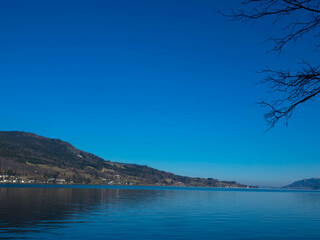 Attersee lake at Salzkammergut area in Austria.  Tree branches, beautiful blue sky and the alps mountains. Upper Austria, Europe