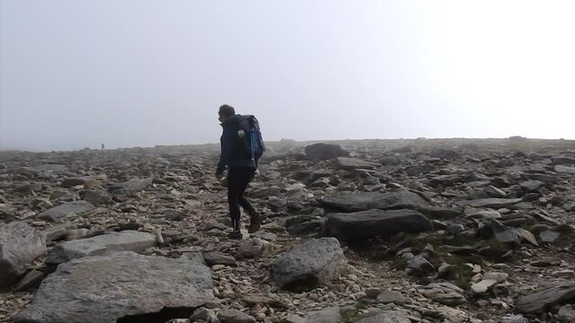 Man hiking with a backpack on summit of a misty and rocky Glyder Fawr mountain in Snowdonia National Park, Wales