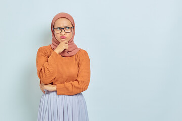 Naklejka premium Pensive young Asian Muslim woman in brown sweater and glasses, holding chin while thinking something isolated on white background. people religious lifestyle concept