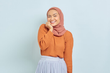 Cheerful young Asian Muslim woman in brown sweater and putting palms on chin isolated over white background. Muslim lifestyle concept