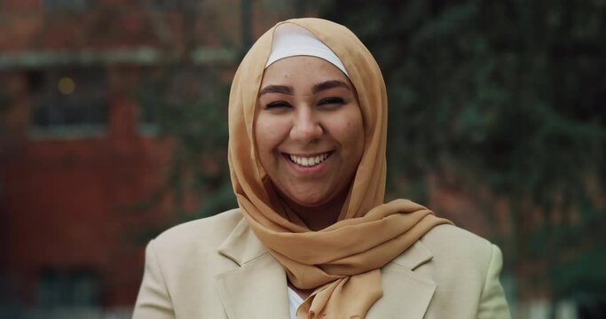 Cinematic shot of young happy Arabian muslim woman wearing hijab is smiling  in camera outdoors.