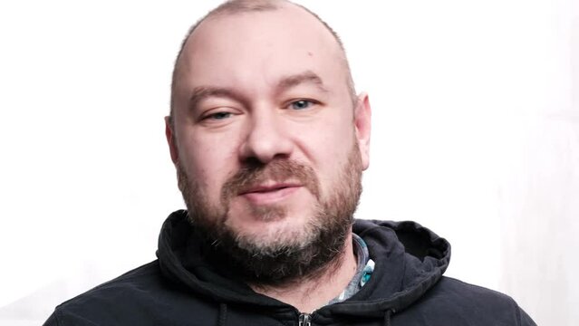 The man speaks amiably to the camera. White background. A middle-aged man, forty years old. Unshaven man.