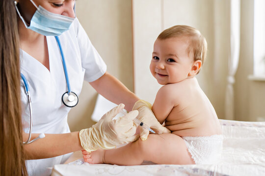 Young female pediatrician or nurse giving an intramuscular injection of a vaccine to leg of little baby boy Immunization for children concept. Happy little cute boy getting a flu shot not afraid of
