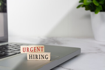 Urgent hiring text on wooden block cube placed on laptop or notebook.
