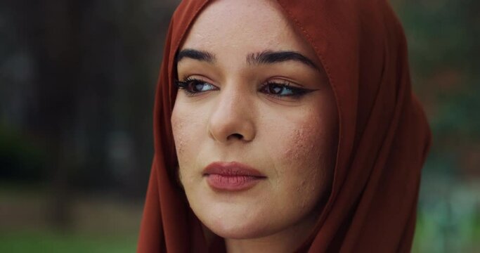 Cinematic close up shot of young happy Arabian muslim woman wearing hijab is looking around her and smiling  in green public city park.