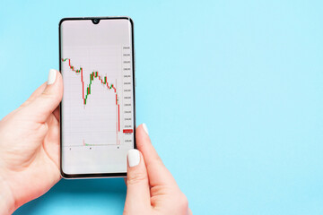 Female hand holding a phone with a stock market graph on blue background.