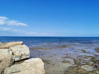 Large stones, long-hardened lava, the shore of the Mediterranean Sea against the backdrop of the sea and a blue sky with clouds.