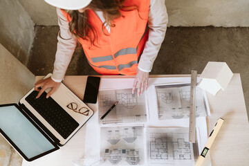 top view of professional architect woman in construction site working on laptop and blueprints