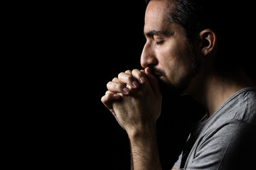 The man folding his hands in prayer to god on a black background. prayer to God for happiness and a better life. Repent of your sins. Unity with God