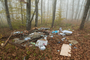 Construction and plastic trash lying in the foliage in the foggy forest. Pollution of the environment. Environmental problems. Toilet, plumbing fixtures and boards in autumn leaves in nature
