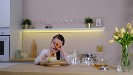 Happy little baby girl smiles happily when she eats cookies sitting at table in kitchen at home. Funny baby hunts for delicious cookies - Powered by Adobe