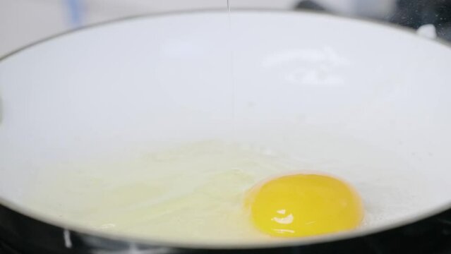 Egg yolk dropping into white cooking skillet and splashing in slow motion 4k close up for breakfast