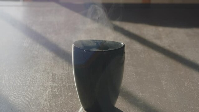 Reeking cup of hot morning coffee at sunrise. Static shot in slow motion.