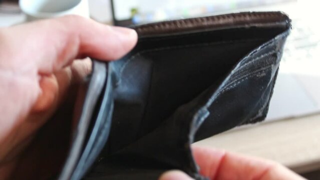 Hands opening an empty brown leather wallet in front of a bright office backdrop. Static close up footage