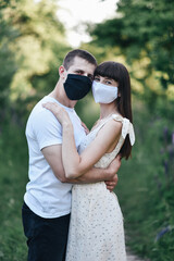 Young beautiful couple in black and white masks during the Coronavirus pandemic in nature