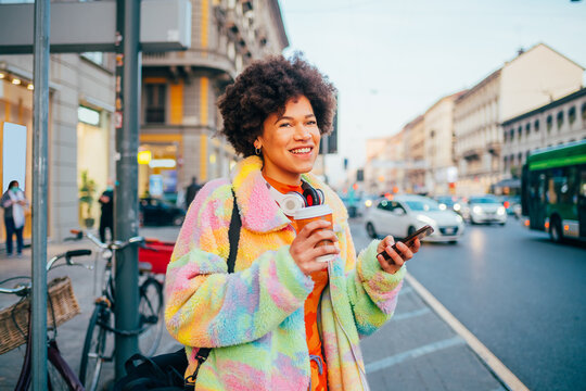 Young black curly smiling woman outdoor holding reusable cup using smartphone