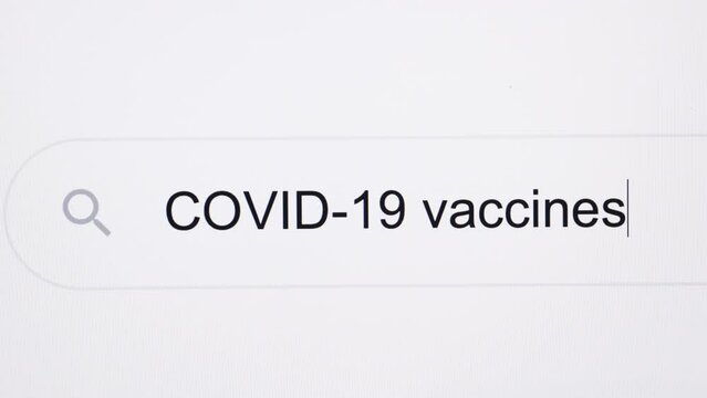 Typing the word COVID 19 vaccines in the browser and clicking the search button on a pixelated computer screen. COVID-19 vaccines - Internet browser search bar typing coronavirus information research
