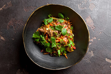 beef wok noodles with vegetables and sesame on black bowl top view