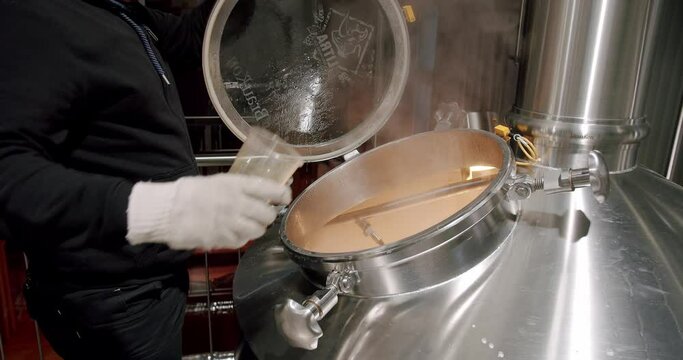 Pouring Malt Grains Into The Large Milling Tank In The Brewery. Beer making in craft brewery, Kettle with beer inside. Modern beer factory. Huge steel tanks for beer brewing.