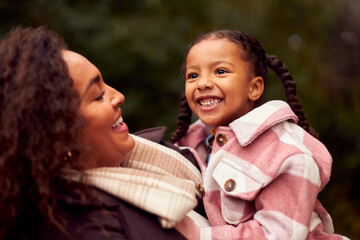 Loving Mother Carrying Daughter On Family Walk Through Autumn Countryside Together