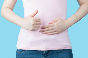 Close up of healthy woman touching her abdomen and showing thumb up sign for good digestive, healthy gut, probiotics, slim fit body and gynecology concept.