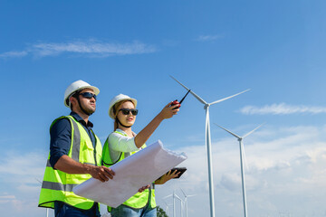 Asian man and woman engineers working on site with copy space in wind turbine on the background....