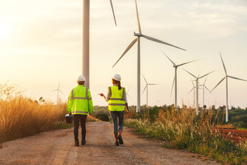 Back view of young maintenance engineers team working in wind turbine farm at sunset.
