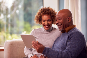 Senior Couple Sitting On Sofa At Home Using Digital Tablet Watching Streaming Movie Together