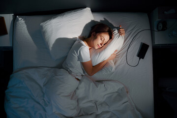Young woman hugging pillow in bed, top view.