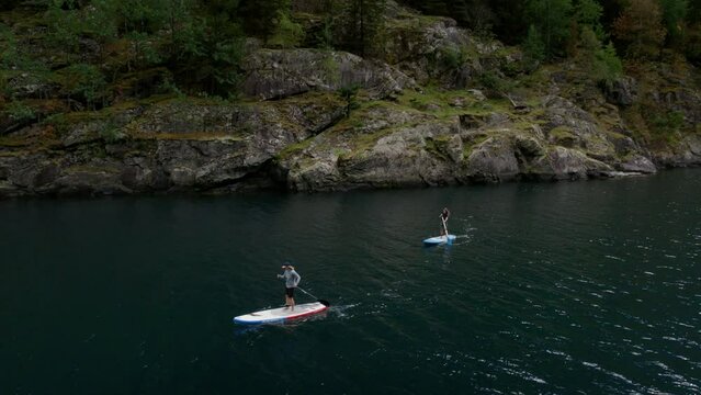 Active people friends standing up paddle boards in epic splendid beautiful glacier fjord in western norway. Drone view on trendy healthy lifestyle activity and travel meditative Scandinavia experience