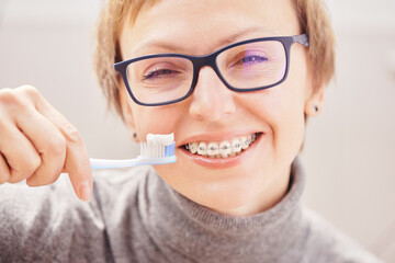 Stylish and beautiful young blonde woman in glasses and a gray sweater in braces and smiling on a white background, dentist orthodontist concept