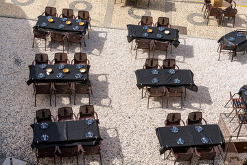 high angle view of many empty restaurant tables with black tablecloths and place settings in an...