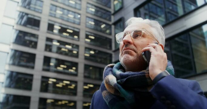 A gray-haired man uses a mobile phone, standing in business center of the city