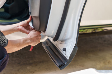 Mechanic man using wedge unpack vehicle door part for check damage in garage